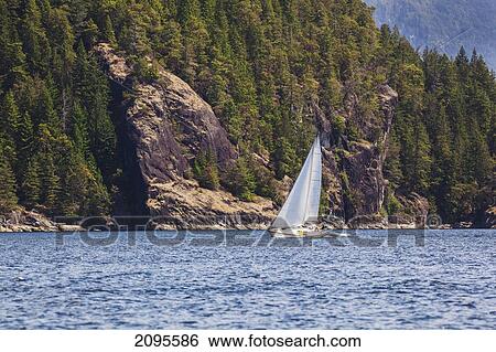 Stock Photograph - A Man Sails His Sailboat In Desolation Sound; British Columbia Canada. Fotosearch