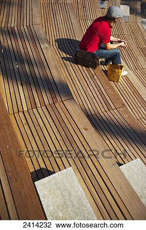 Stock Image - A man sits alone on tiered wooden benches; Barcelona, Spain. Fotosearch