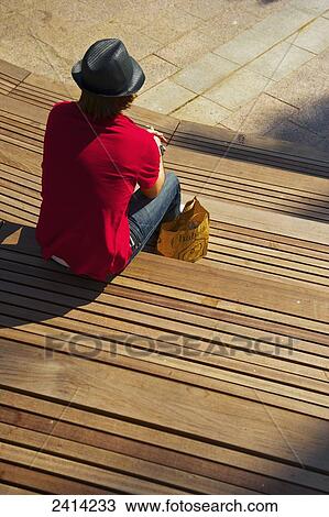Stock Image - A man sits alone on tiered wooden benches; Barcelona, Spain. Fotosearch