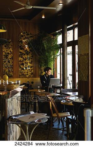 Picture - A man sits at a table in a cafe with his laptop computer, staring out the window, Marais district; Paris, France. Fotosearch
