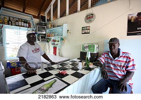 Stock Image - A man sits at the counter of the Bequia Island Rum shop; Port Elizabeth, St. Vincent and the Grenadines. Fotosearch