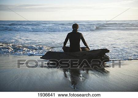 Stock Image - A Man Sits On A Piece Of Driftwood On The Wet Shore Looking Out At The Water; La Push Washington United States Of America. Fotosearch