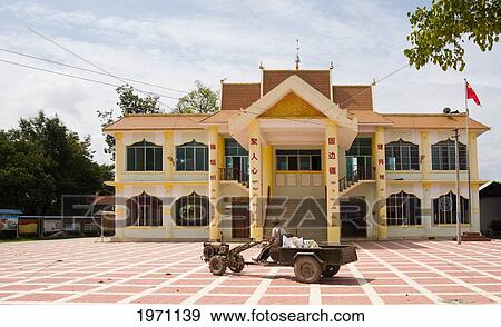 Stock Photo - A Man Sits On A Vehicle Parked In Front Of A Yellow Building With The China Flag; Ruili Yunnan China. Fotosearch