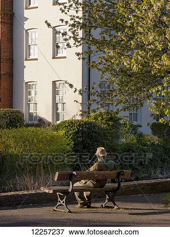 Stock Photo - A man sits on a wooden bench; Wiltshire, Salisbury, England. Fotosearch