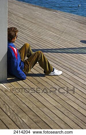 A man sits on a wooden promenade at the water's edge; Barcelona, Spain View Large Photo Image Picture - A man sits on a wooden promenade at the water's edge; Barcelona, Spain. Fotosearch
