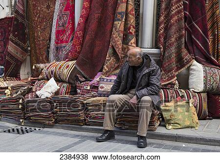 Stock Photo - A man sits on piles of textiles in the street; Istanbul, Turkey. Fotosearch