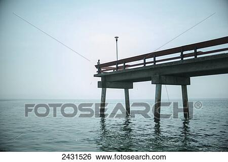 Stock Photograph - A man sits on the end of a pier on the north side of Toronto Island; Toronto, Ontario, Canada. Fotosearch
