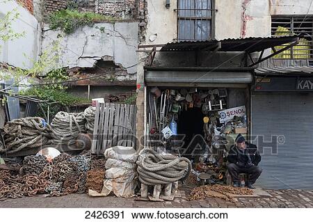 Stock Image - A man sits outside a shop with piles of chain and rope; Istanbul, Turkey. Fotosearch
