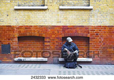 A man sits reading a newspaper against a brick building; London, England View Large Photo Image Stock Image - A man sits reading a newspaper against a brick building; London, England. Fotosearch