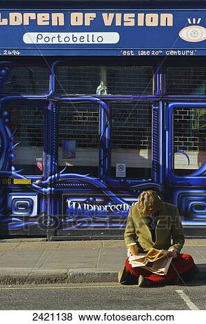 Stock Photo - A man sits reading a newspaper on the side of the street, Portobello Road Market; London, England. Fotosearch