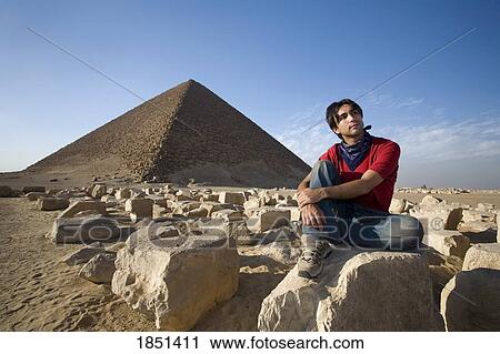Stock Image - A Man Sitting Near A Pyramid In The Desert. Fotosearch