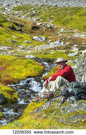 Stock Photography - A man sitting next to a stream, Kenai Fjords National Park, Kenai Penninsula, Southcentral Alaska. Fotosearch