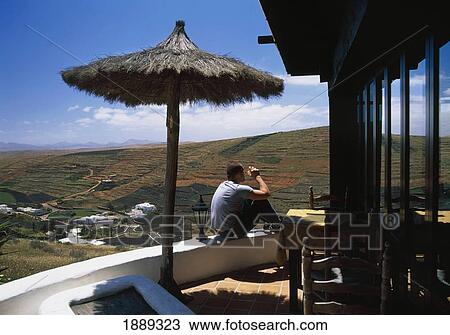 Stock Image - A Man Sitting On A Balcony Overlooking The Fields Of Lanzarote.. Fotosearch