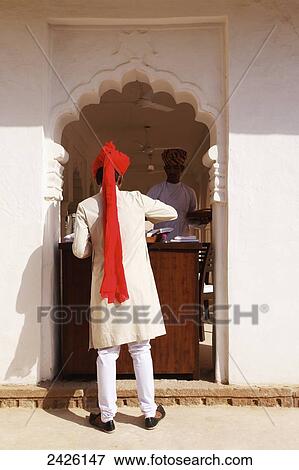 Stock Photo - A man standing at the concierge desk in a scalloped entrance at Ranvas Palace; Rajasthan, India. Fotosearch