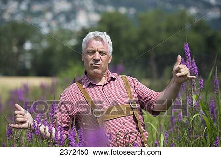Stock Image - A Man Standing In A Field With Purple Blossoms Giving The Shaka Sign With His Hands; Locarno, Ticino, Switzerland. Fotosearch