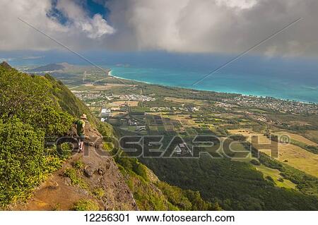 A man standing on the edge of a cliff on the Kuliouou Ridge Trial enjoys the view of Oahu's windward side and the town of Waimanalo as the clouds roll in on a summer's day; Waimanalo, Oahu, Hawaii, United States of America View Large Photo Image Stock Image - A man standing on the edge of a cliff on the Kuliouou Ridge Trial enjoys the view of Oahu's windward side and the town of Waimanalo as the clouds roll in on a summer's day; Waimanalo, Oahu, Hawaii, United States of America. Fotosearch