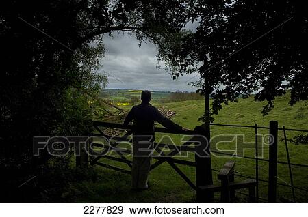 Stock Photo - A man stands at a fence viewing the surrounding countryside at Rockingham Castle; Leicestershire, England. Fotosearch