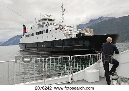 A Man Stands At The Stern Of A Boat Watching A Ship Pass In The Waterway; Sognefjord Norway View Large Photo Image Stock Image - A Man Stands At The Stern Of A Boat Watching A Ship Pass In The Waterway; Sognefjord Norway. Fotosearch