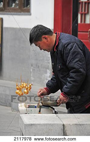 Stock Photo - A Man Stands In The Street Dipping Objects On A Stick To Colour Them Gold; Beijing China. Fotosearch