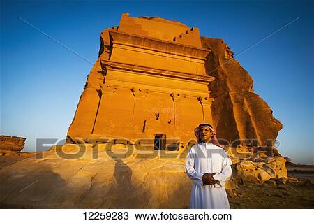 Stock Image - A man stands outside a rock-cut building; Medain Saleh, Saudi Arabia. Fotosearch