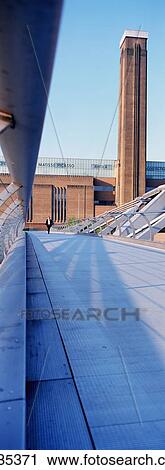 Stock Image - A Man Walking Across The Millennium Bridge With The Tate Modern Behind. Fotosearch