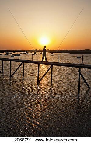 A Man Walks On A Pier With Boats Moored In The Water At Sunset Near Faro; Algarve Portugal View Large Photo Image Stock Image - A Man Walks On A Pier With Boats Moored In The Water At Sunset Near Faro; Algarve Portugal. Fotosearch