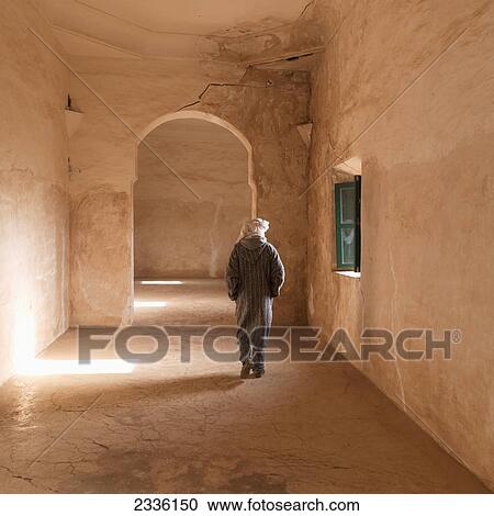 Stock Image - A Man Walks Through A Corridor With A Crack In The Archway; Telouet, Souss-Massa-Draa, Morocco. Fotosearch