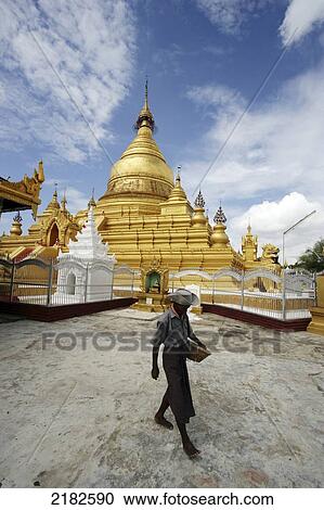 Stock Image - A man walks with Kuthodaw Pagoda in the background; Mandalay, Burma. Fotosearch