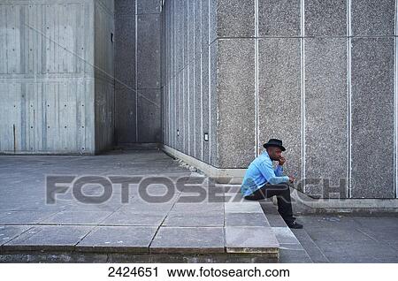 A man wearing a blue shirt and hat sits on a step beside a concrete wall, Southbank; London, England View Large Photo Image Stock Image - A man wearing a blue shirt and hat sits on a step beside a concrete wall, Southbank; London, England. Fotosearch