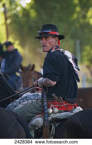 Picture - A man wearing hat, scarf and colourful belt sitting on a horse; Malargue, Argentina. Fotosearch