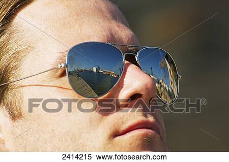 Stock Photography - A man wearing sunglasses with the promenade reflected in the lenses; Barcelona, Spain. Fotosearch