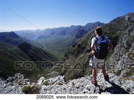 Stock Photography - A Man With A Backpack Stands On A Mountain Ridge Looking Out Over The Valley And Range. Fotosearch