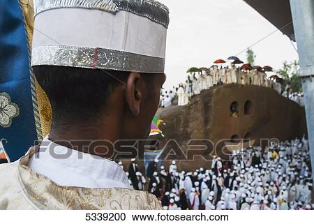 A man with traditional hat and clothing trimmed in silver and gold with a group of people in white garments in the distance; Lalibela, Ethiopia View Large Photo Image Stock Image - A man with traditional hat and clothing trimmed in silver and gold with a group of people in white garments in the distance; Lalibela, Ethiopia. Fotosearch