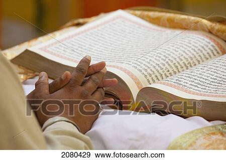 Stock Photo - A Man's Hands Folded In Front Of A Large Open Book; Ludhiana, Punjab, India. Fotosearch