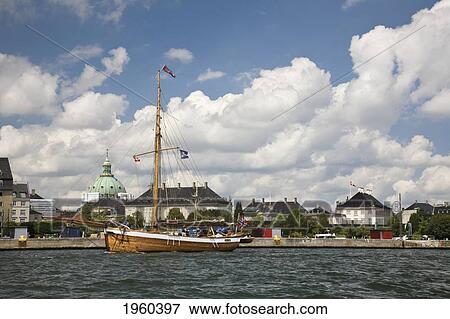 Stock Photo - A Moored Sailboat And Buildings Along The Coast; Copenhagen, Denmark. Fotosearch