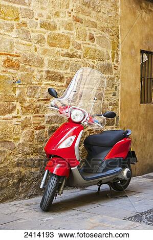 Stock Image - A motor scooter parked beside a stone wall; Barcelona, Spain. Fotosearch