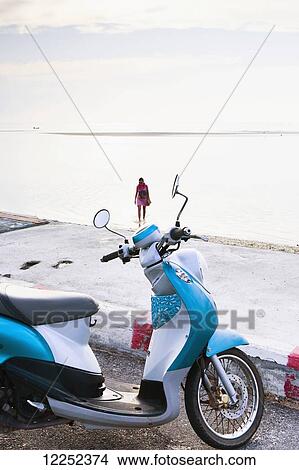 Picture - A motor scooter parked on the side of the road at the water's edge, Nathon Beach; Nathon, Ko Samui, Thailand. Fotosearch