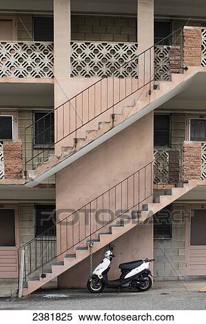 Stock Photography - A motor scooter sits under a staircase leading up a residential building; Honolulu, Oahu, Hawaii, United States of America. Fotosearch