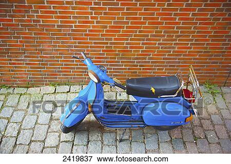 Stock Photo - A motorized scooter parked beside a brick wall; Hamburg, Germany. Fotosearch