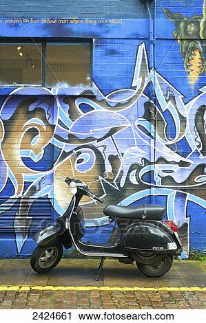 Stock Image - A motorized scooter parked outside a building with abstract artwork painted on the wall, Notting Hill; London, England. Fotosearch