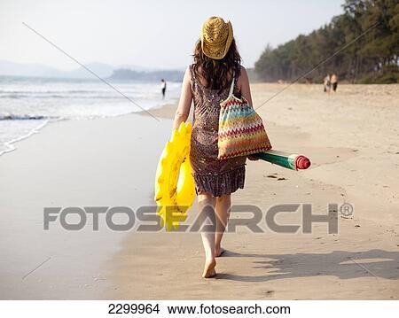 Picture - A mum walks back from beach with inflatable's and beach mat after a day on Turtle Beach, Goa, India.. Fotosearch