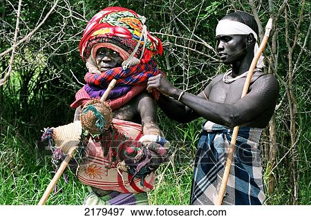 A Mursi tribal man holding his donga (wooden duelling pole) while having his tumoga (duelling kit) fixed during a thagine contest (ceremonial duelling); Makki, Ethiopia View Large Photo Image Stock Photo - A Mursi tribal man holding his donga (wooden duelling pole) while having his tumoga (duelling kit) fixed during a thagine contest (ceremonial duelling); Makki, Ethiopia. Fotosearch