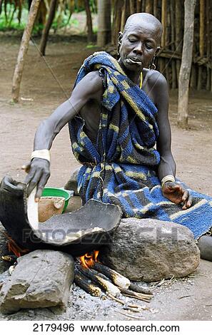 Stock Photograph - A Mursi tribal woman cooking 'tila' (a traditional dish made with maize or sorghum. Makki /South Omo / Southern Nations, Nationalities & People's Region (Ethiopia).. Fotosearch