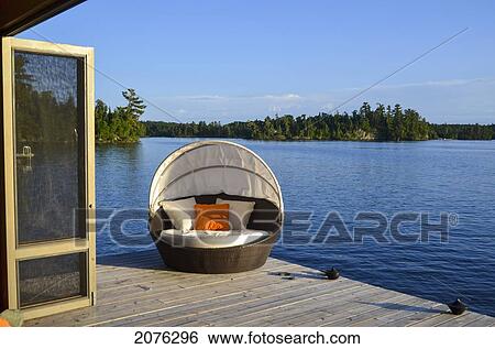 A Padded Lounge Chair On A Wooden Dock At The Water's Edge; Lake Of The Woods Ontario Canada View Large Photo Image Stock Photograph - A Padded Lounge Chair On A Wooden Dock At The Water's Edge; Lake Of The Woods Ontario Canada. Fotosearch