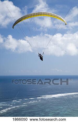 Stock Image - A Paraglider Soars Free Over The Cliffs And Beaches Of The Bukit Peninsula In Bali, Indonesia. Fotosearch