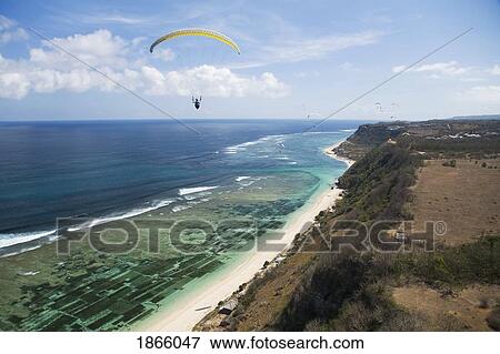 Stock Photo - A Paraglider Soars Free Over The Cliffs And Beaches Of The Bukit Peninsula In Bali, Indonesia. Fotosearch