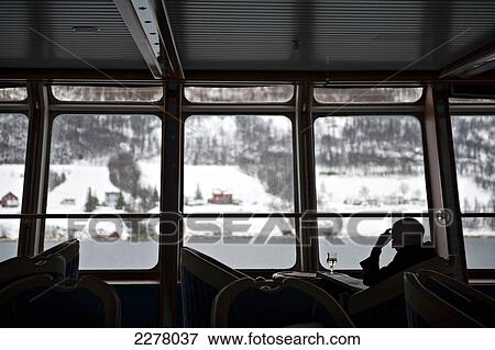 A passenger reads the newspaper in the panoramic lounge of the Hurtigruten ship MS Nordlys as the outside snow covered landscape passes by; Norway View Large Photo Image Stock Photo - A passenger reads the newspaper in the panoramic lounge of the Hurtigruten ship MS Nordlys as the outside snow covered landscape passes by; Norway. Fotosearch