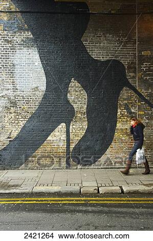 A pedestrian walks by a brick wall with a woman's legs and feet in stilettos painted on the wall, Shoreditch; London, England View Large Photo Image Picture - A pedestrian walks by a brick wall with a woman's legs and feet in stilettos painted on the wall, Shoreditch; London, England. Fotosearch
