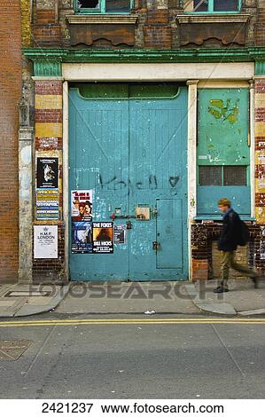 Stock Photo - A pedestrian walks by a large blue door with posters, Shoreditch; London, England. Fotosearch