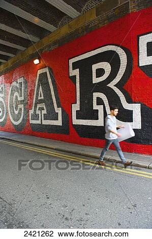A pedestrian walks on the street along a wall with large lettering painted on, Shoreditch; London, England View Large Photo Image Stock Image - A pedestrian walks on the street along a wall with large lettering painted on, Shoreditch; London, England. Fotosearch
